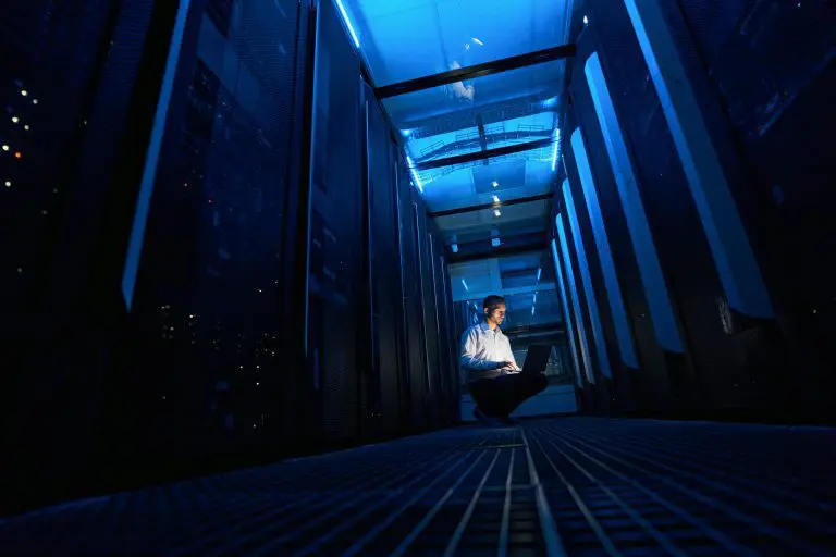 Male server administrator squatting with laptop in server room