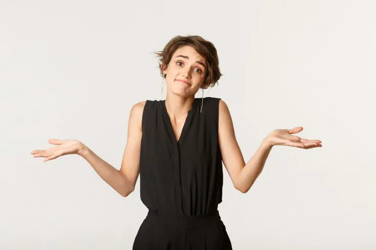 Clueless young woman apologizing for being unaware, shrugging with awkward smile, standing white