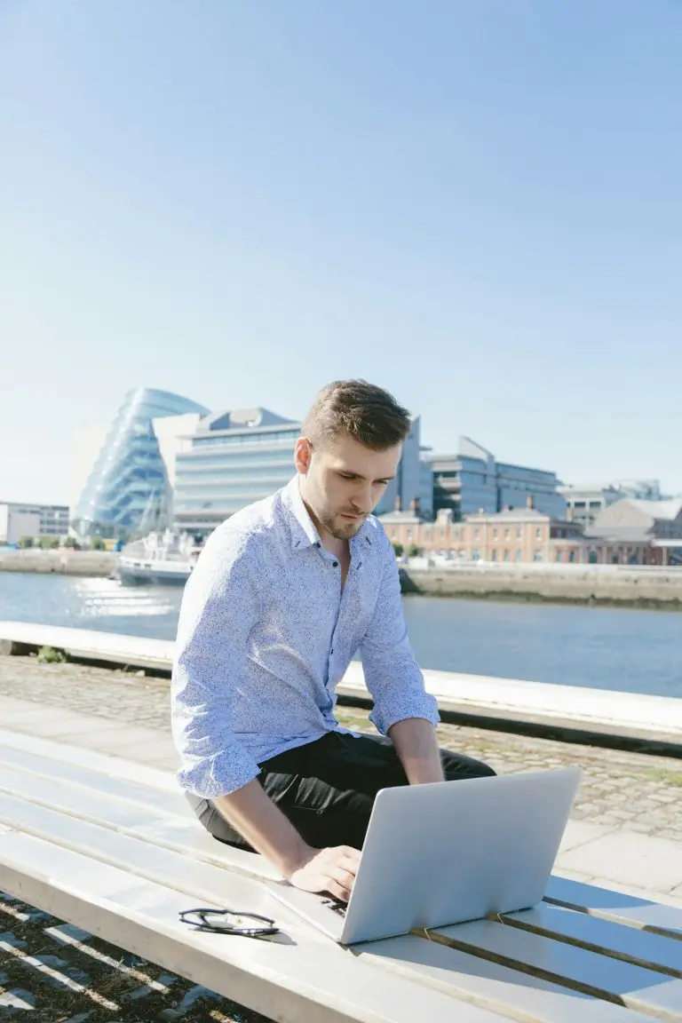 Ireland, Dublin, young businessman sitting on bench using laptop