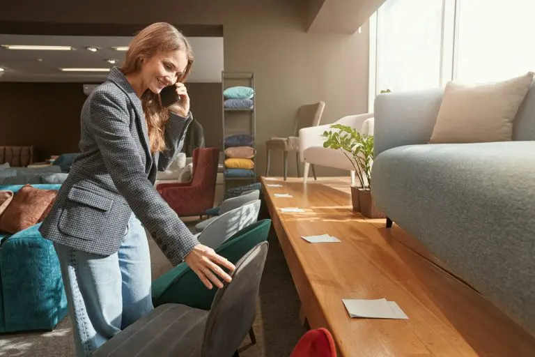 Joyous lady with smartphone choosing chair in shop